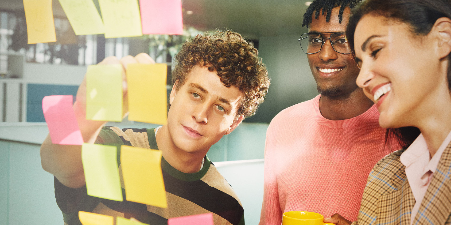 Ein junger Mitarbeiter und zwei erfahrenere Mitarbeiter:innen brainstormen bei Wüstenrot vor einer Postit-Wand